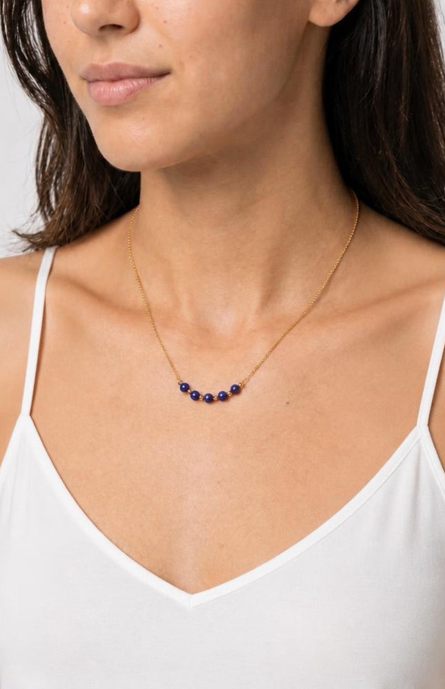 A three-quarter angled profile view of the model in natural light, showcasing the vibrant pop of the deep blue lapis beads against a warm-weather outfit.