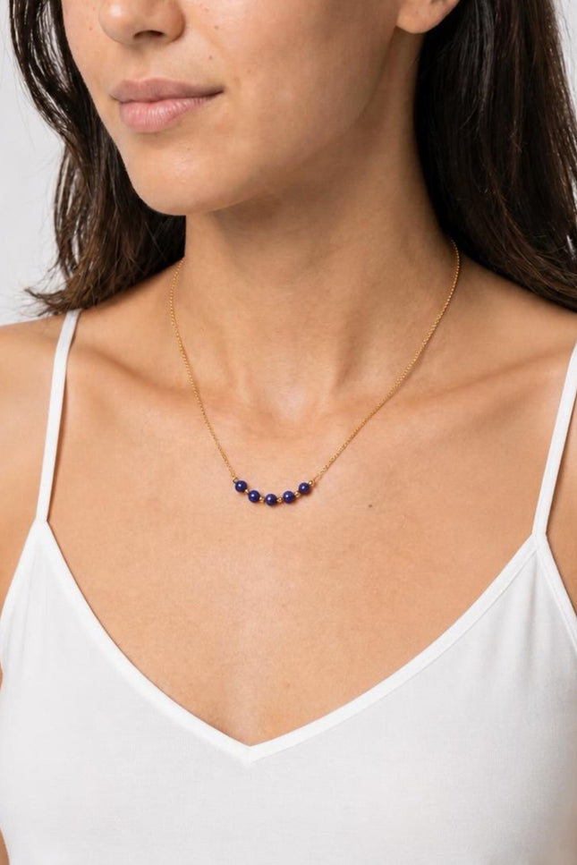A three-quarter angled profile view of the model in natural light, showcasing the vibrant pop of the deep blue lapis beads against a warm-weather outfit.