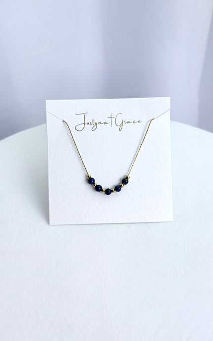 A dainty gold twisted chain necklace with alternating deep blue lapis lazuli beads beautifully arranged on a clean boutique display card, highlighting the rich color contrast.