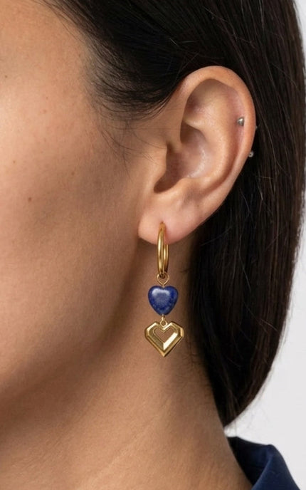 A close-up, macro shot angled view of the model wearing the double heart earrings, capturing how the polished gold charms catch the light from the side.