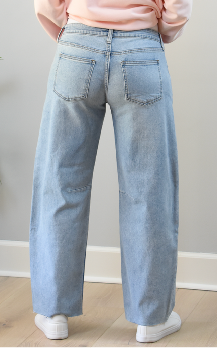 Person wearing light blue jeans and a pink top in a minimal indoor setting.