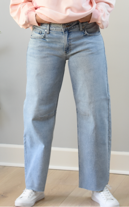 Person wearing light blue jeans and a pink sweatshirt against a neutral background