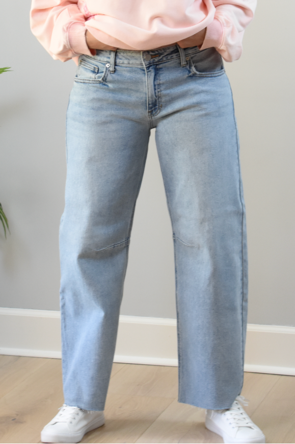 Person wearing light blue jeans and a pink sweatshirt against a neutral background