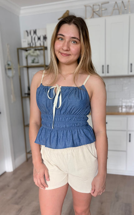 Lightweight denim cami with a shirred bodice, front tie detail, and soft peplum hem in a breathable cotton-blend fabric for summer styling
