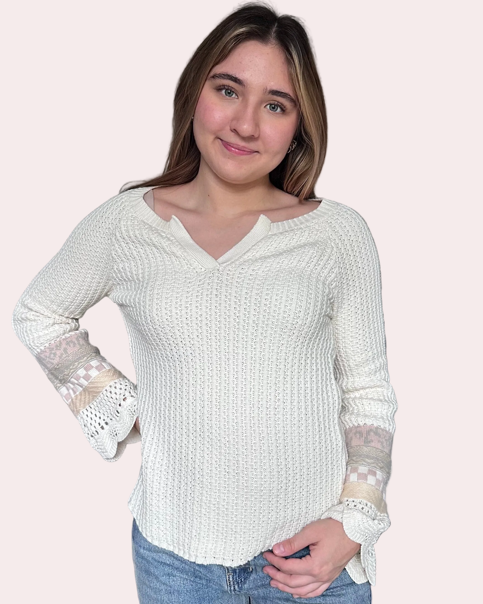Woman wearing a white textured sweater with lace sleeves on a light pink background