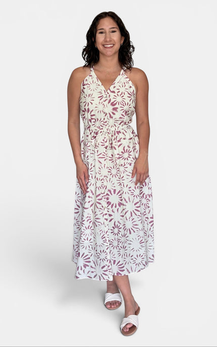 A woman modeling a sleeveless halter-neck midi dress with an allover white and dusty rose floral pattern, paired with white slide sandals, against a light gray studio background.
