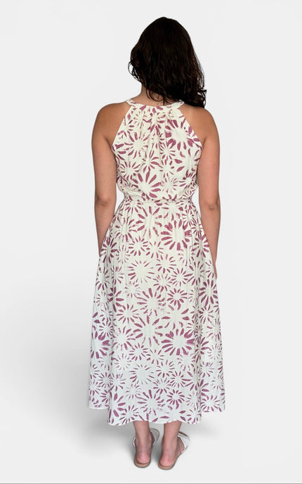 A woman viewed from the back wearing a sleeveless halter-neck midi dress with an allover white and dusty rose floral pattern, set against a plain light gray studio background.