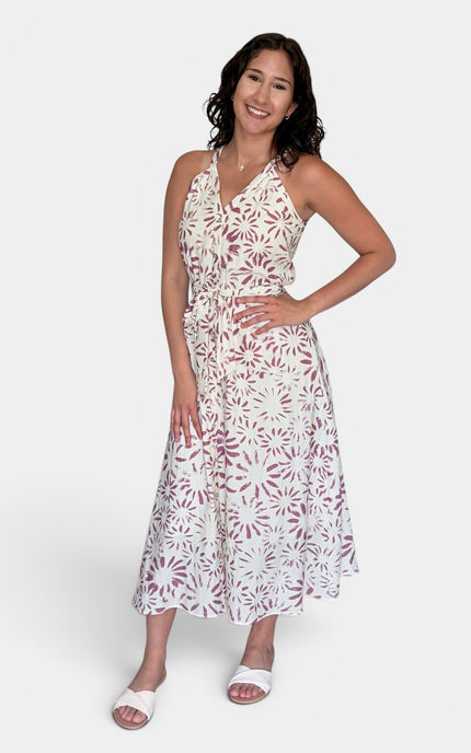 A woman modeling a sleeveless white halter midi dress with a dusty rose floral pattern, paired with white slide sandals, against a light gray studio background.