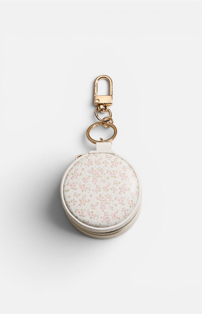 Top view of a compact, round mini jewelry case featuring a soft pink floral design on a smooth white exterior with an elegant gold-tone zipper.