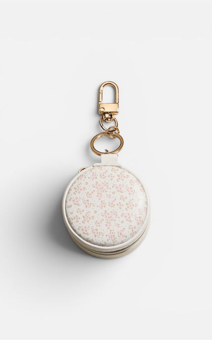 Top view of a compact, round mini jewelry case featuring a soft pink floral design on a smooth white exterior with an elegant gold-tone zipper.