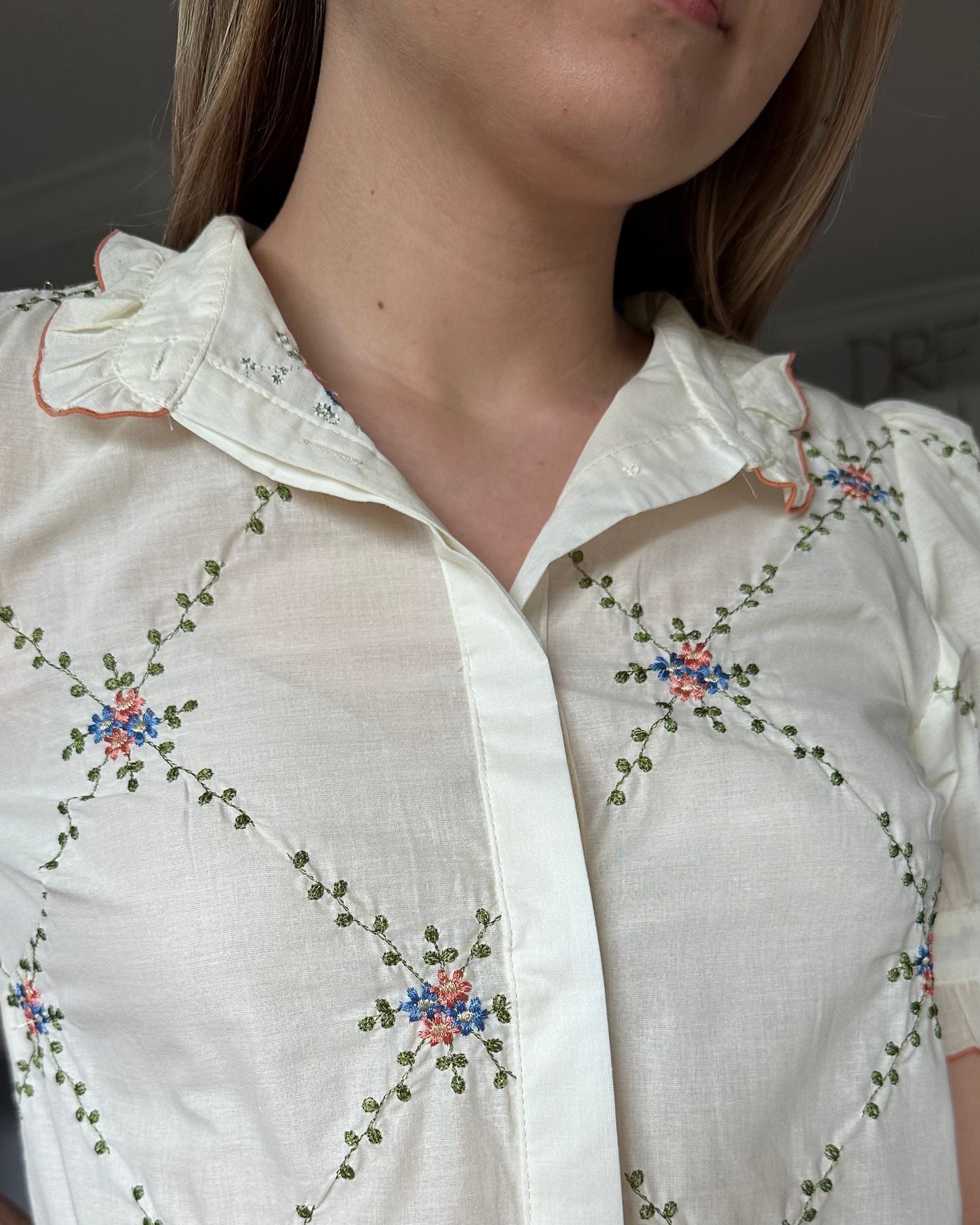 Close-up of the Noemi blouse ruffle collar with contrast edging and floral embroidered detail