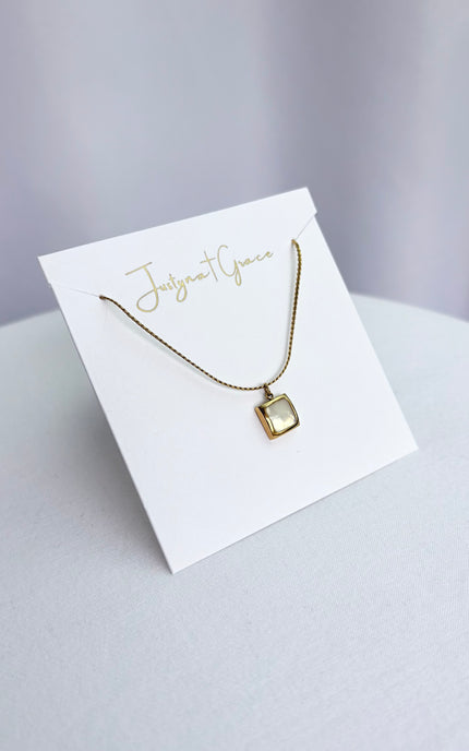 A polished square gold pendant necklace with a natural white sea shell inlay displayed on a clean boutique jewelry card, highlighting the detailed twisted rope chain and the high-shine finish of the 18k gold PVD plating.