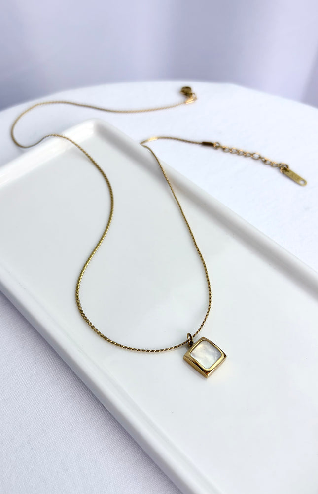 Flat lay view of an 18k gold PVD plated stainless steel necklace featuring a square pendant with a genuine white sea shell inlay and a classic twisted rope chain.