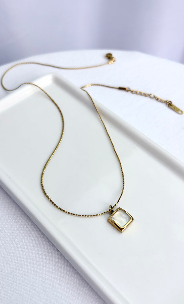 Flat lay view of an 18k gold PVD plated stainless steel necklace featuring a square pendant with a genuine white sea shell inlay and a classic twisted rope chain.