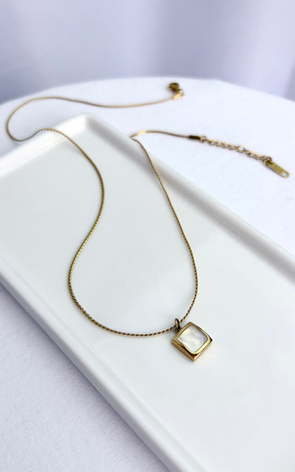 Flat lay view of an 18k gold PVD plated stainless steel necklace featuring a square pendant with a genuine white sea shell inlay and a classic twisted rope chain.
