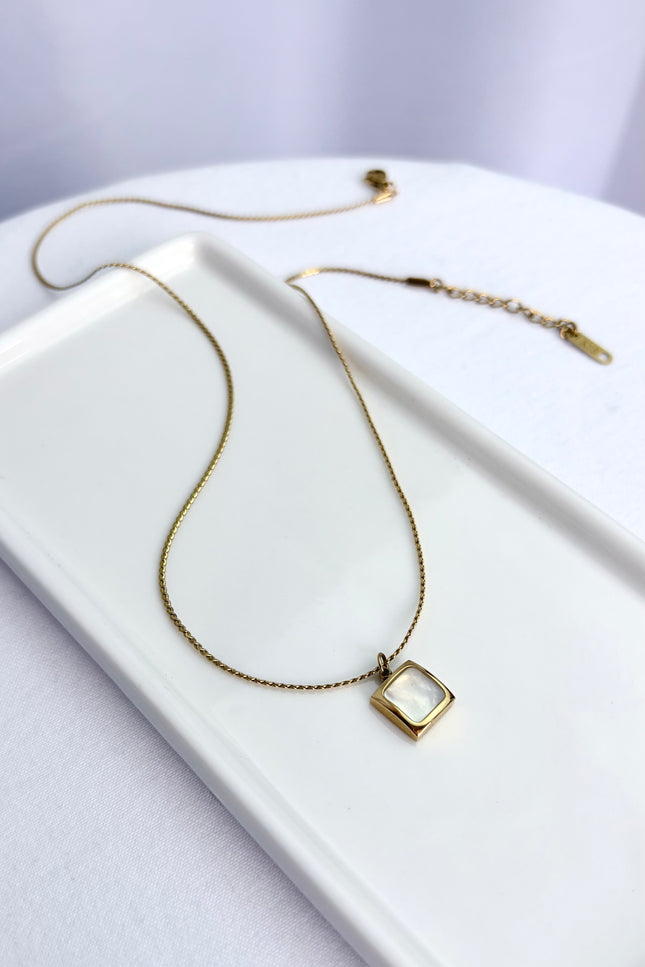 Flat lay view of an 18k gold PVD plated stainless steel necklace featuring a square pendant with a genuine white sea shell inlay and a classic twisted rope chain.
