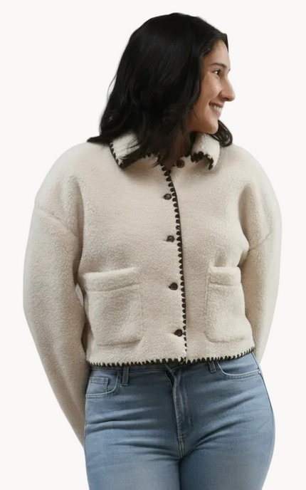 Woman wearing a beige  sherpa coat with black trim on a white background