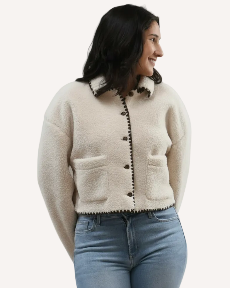 Woman wearing a beige  sherpa coat with black trim on a white background