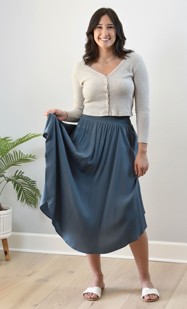 Woman holding a blue skirt indoors with a plant in the background