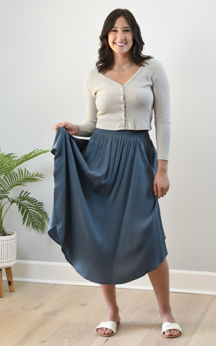 Woman holding a blue skirt indoors with a plant in the background