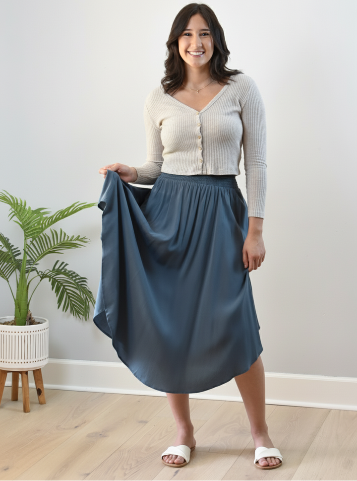 Woman holding a blue skirt indoors with a plant in the background