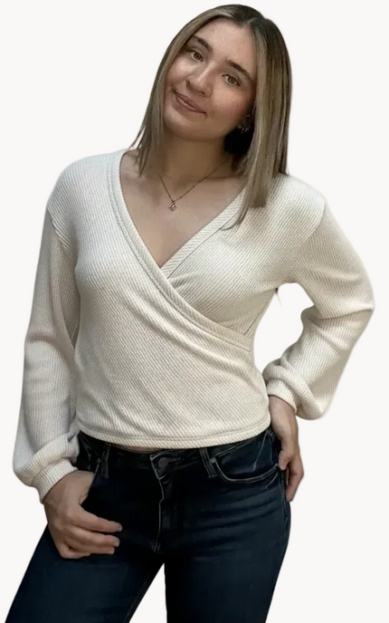 Woman wearing a cream sweater and dark jeans on a light pink background