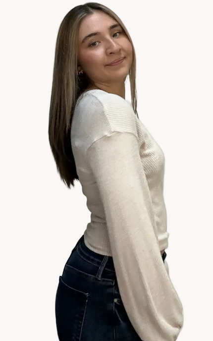 Woman wearing a white long-sleeve top and dark jeans on a light pink background
